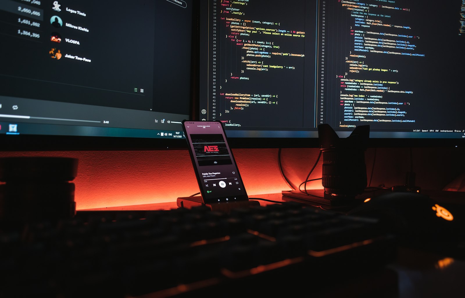 Smartphone on a developer desk in front of monitors filled with source code